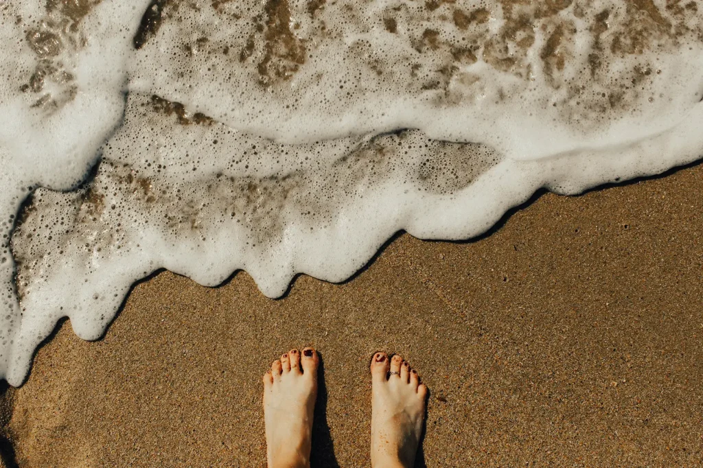 toes standing on a beach about to get wet from a wave.